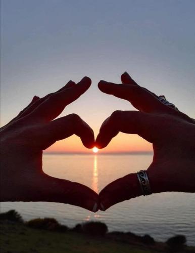 two hands in the shape of a heart in front of a sunset at Y Bwthyn Bach Cute Stone Cottage in Tywyn in Tywyn