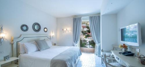 a white bedroom with a bed and a desk and a window at Villa Il Canto - Homelike Villas in Positano