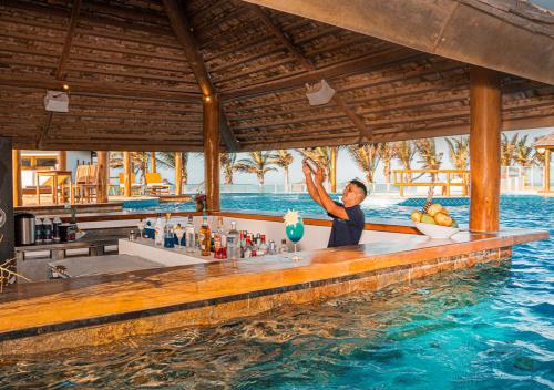 un hombre parado en un bar en el agua en The Coral Beach Resort by Atlantica, en Trairi