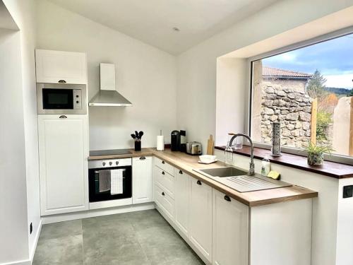 a kitchen with white cabinets and a large window at Superbe appartement avec jacuzzi et jardin privé in Marlhes