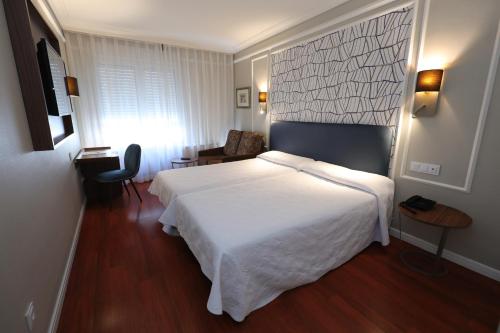 a bedroom with a large white bed and a desk at Hotel Corona de Castilla Burgos in Burgos