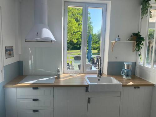 een witte keuken met een wastafel en een raam bij Le cottage des Vaux avec cheminée, sauna et jacuzzi dans un parc arboré in Senlisse