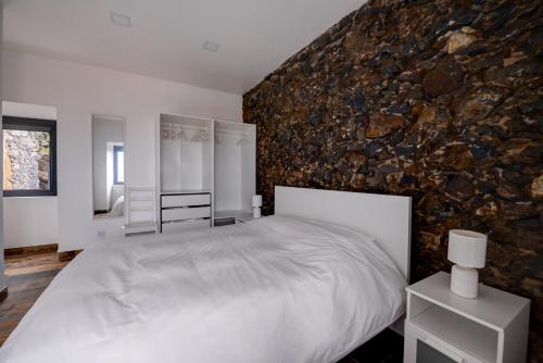 a bedroom with a white bed and a stone wall at Fontinha Terrace View House in Faja Grande
