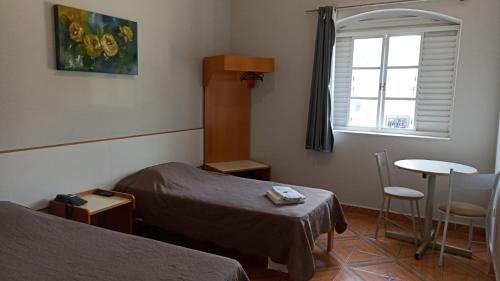 um quarto com duas camas e uma mesa e uma janela em Victoria Hotel - Campanha - MG em Campanha