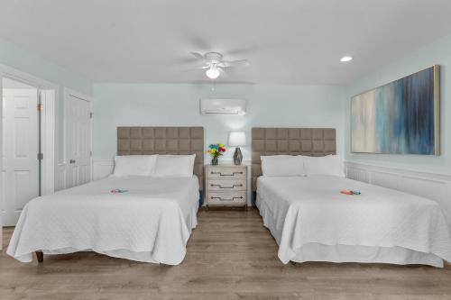 two beds in a bedroom with white walls and wood floors at Loggerhead Inn and Suites in Surf City