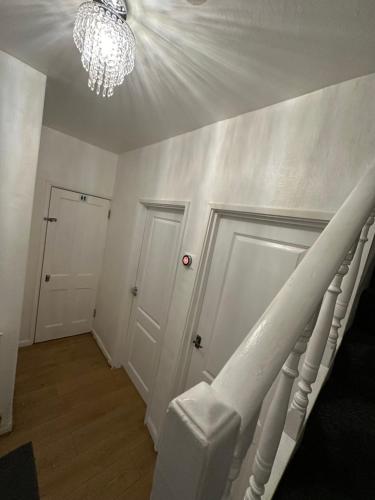 a white hallway with a staircase and a chandelier at Double Room With Free WiFi Keedonwood Road in Bromley
