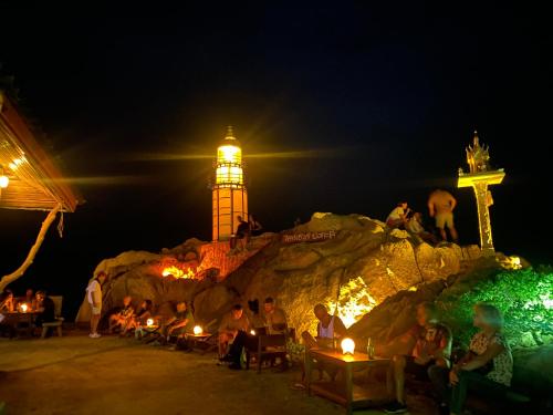a group of people sitting at tables with a lighthouse at night at Lighthouse Bungalows in Haad Rin