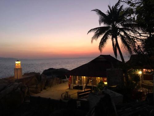 a palm tree and a building on the beach at sunset at Lighthouse Bungalows in Haad Rin