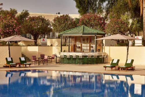 a swimming pool with chairs and a gazebo with a table and umbrella at Fes Marriott Hotel Jnan Palace in Fès