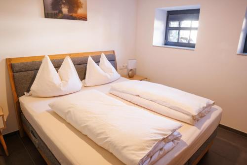 um quarto com uma cama com lençóis brancos e almofadas em Ferienwohnung Alter Kuhstall em Neuenstein