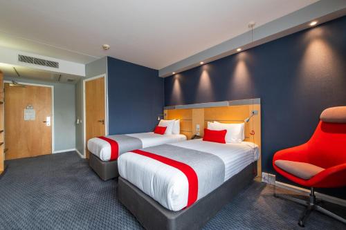 a hotel room with two beds and a red chair at Holiday Inn Express Ramsgate – Minster by IHG in Ramsgate