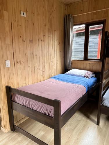 a small bed in a wooden room with a window at QUELEN AUSTRAL in Hornopiren