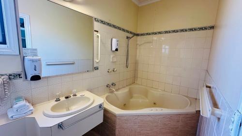 a bathroom with a tub and a sink and a mirror at Early Australian Motor Inn in Mildura