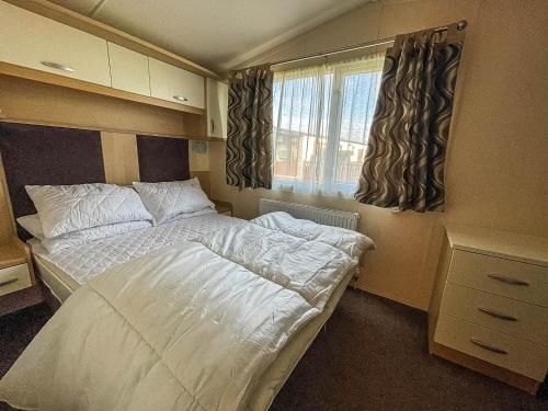 a small bedroom with a bed and a window at Lovely Caravan With Spacious Decking At North Denes In Suffolk, Ref 40134nd in Lowestoft
