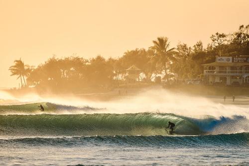 two people riding a wave on surfboards in the ocean at Surf Shack in Iconic Rainbow Bay - Coolangatta QLD (pet friendly) in Gold Coast