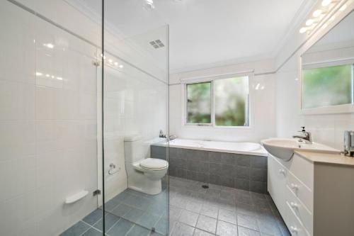 a white bathroom with a shower and a toilet and a sink at Holley House in Leura
