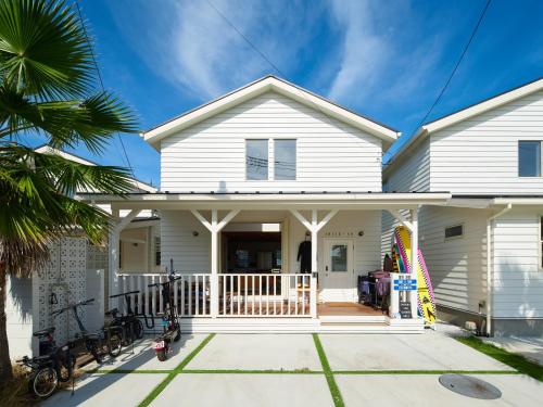 a white house with a porch and a palm tree at Surf & Turf Ichinomiya East - 九十九里 サーフ&ターフ一宮イースト in Ichinomiya