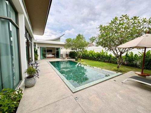 a swimming pool next to a house with an umbrella at Lada Pool Villa in Bang Tao Beach