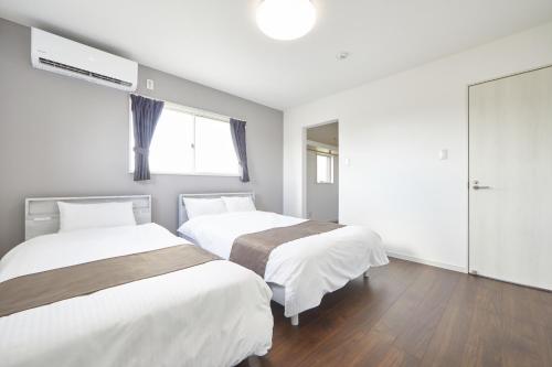 瀬底にあるvilla PILINAの白い壁とウッドフロアの客室で、ベッド2台が備わります。