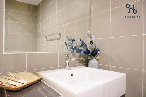 a bathroom with a white sink and a vase of flowers at Homesuite' Home at Aeropod SOVO in Kota Kinabalu