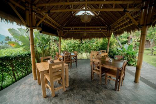 a restaurant with wooden tables and chairs under a roof at Kubu Sakian Villa and Restaurant Sidemen in Silebeng
