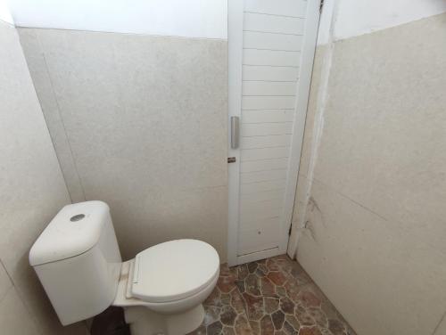 a white bathroom with a toilet and a door at SPOT ON 93367 Wisma Sidosari Syariah in Lampung