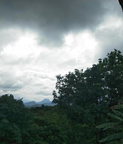 een bewolkte hemel met bomen en bergen op de achtergrond bij Nature's Nest Homestay in Kegalle