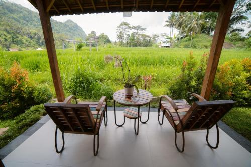 a patio with a table and chairs and a field at Kubu Sakian Villa and Restaurant Sidemen in Silebeng