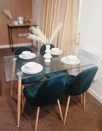 un tavolo in vetro con sedie e piatti di Jesse 2 Bedroom Apartment by GET a Dunstable