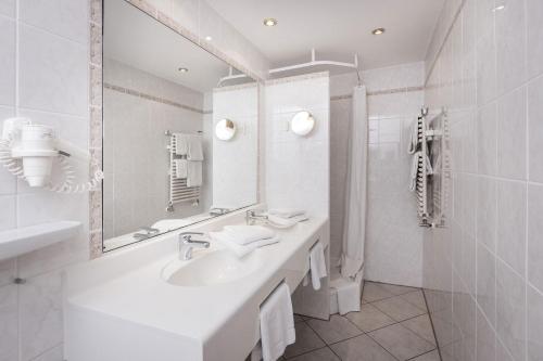 ein weißes Badezimmer mit einem Waschbecken und einem Spiegel in der Unterkunft Allgäuer Bergbad in Oberstdorf