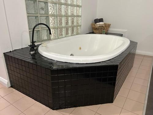 a large bath tub with a black tiled floor at Country 2 Coast Motor Inn Coffs Harbour in Coffs Harbour