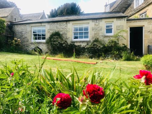 a house with red flowers in front of a yard at The Old Post Office Studio Apartment in a Beautiful Cotswold Village in Cirencester