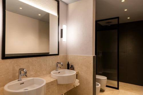 a bathroom with two sinks and a mirror and a toilet at Hotel Le Dune Piscinas in Ingurtosu