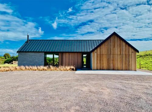 a wooden house with a black roof on a field at Rusty Ram Luxury Lodge in Haruru