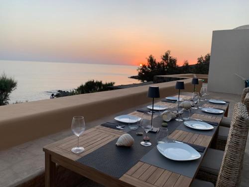 - une table en bois avec des assiettes et des verres à vin et l'océan dans l'établissement Villa calypso Pantelleria, à Pantelleria