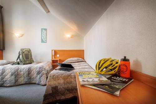 Un dormitorio con 2 camas y una mesa con libros. en Hôtel Compostelle en Lourdes