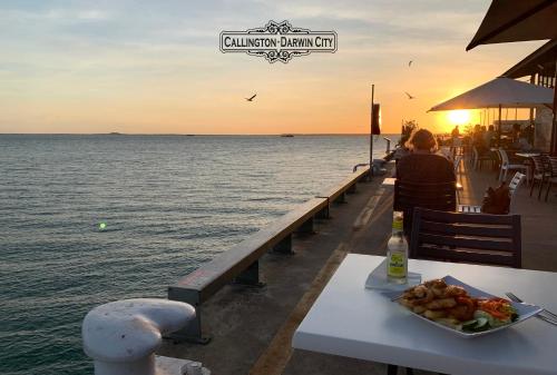 a table with a plate of food next to the ocean at “CALLINGTON” Darwin City @PenthousePads in Darwin