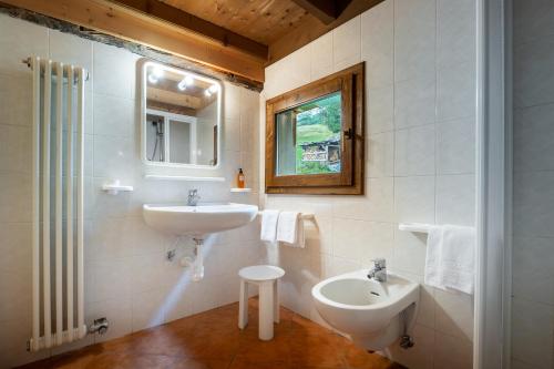 W białej łazience znajduje się umywalka i lustro. w obiekcie Baita Vioz w mieście Peio