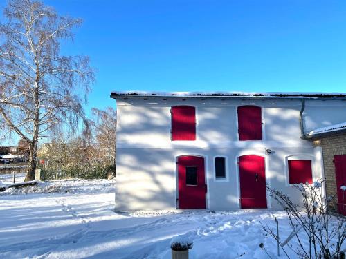 a white house with red doors in the snow at HORAMI Villa - NAMDO Apartment mit Terrasse in Malchow