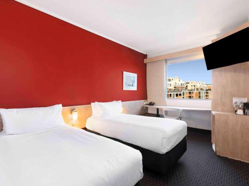 Cette chambre comprend 2 lits et un mur rouge. dans l'établissement ibis Sydney Darling Harbour, à Sydney