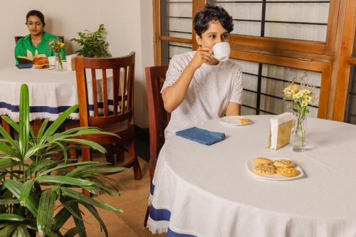 een vrouw aan een tafel die een kop koffie drinkt bij Dutch Manor Boutique Hotel in Cochin