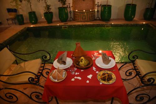 a red table with plates of food next to a swimming pool at Riad Du Petit Prince in Marrakech