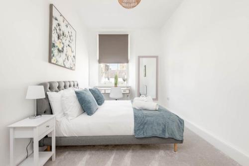 a white bedroom with a large white bed with blue pillows at Skye Sands - The Eden Residence in St. Andrews