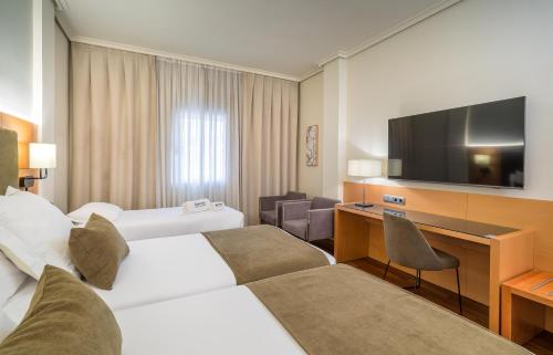 a hotel room with two beds and a desk and a television at Barceló Murcia Siete Coronas in Murcia