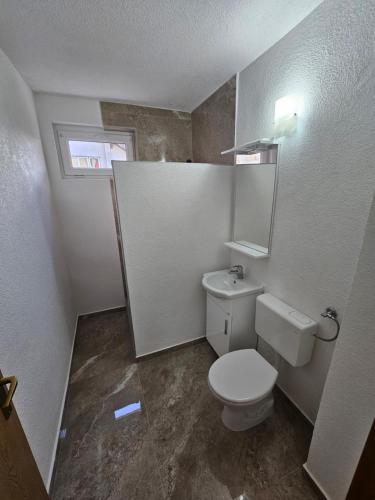 een witte badkamer met een toilet en een raam bij Apartman Capital Novi Grad in Bosanski Novi
