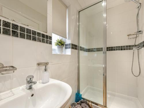 uma casa de banho branca com um lavatório e um chuveiro em Milkwood em Pendine