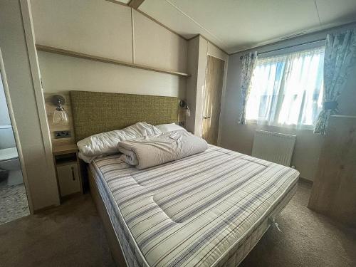 Schlafzimmer mit einem Bett mit weißer Bettwäsche und einem Fenster in der Unterkunft Lovely Caravan With Decking At Carlton Meres Holiday Park In Suffolk Ref 60023ch in Saxmundham