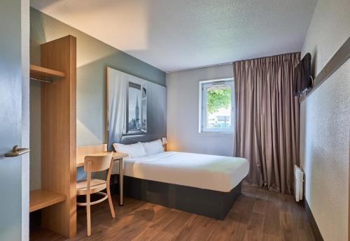 a bedroom with a bed and a desk and a window at B&B HOTEL Caen Mémorial in Caen