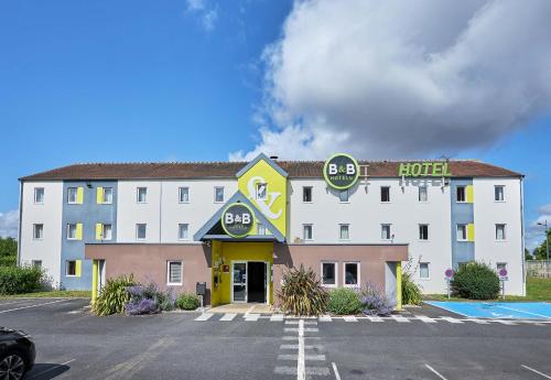 a large white hotel with a parking lot at B&B HOTEL Caen Mémorial in Caen