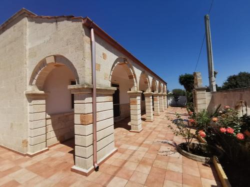贝瓦尼亚圣彼得Villa Vacanze Perla del Salento - Casa Vacanze San Pietro in Bevagna - SALENTO - Puglia - ITALY的一座在庭院中拥有拱门和鲜花的建筑